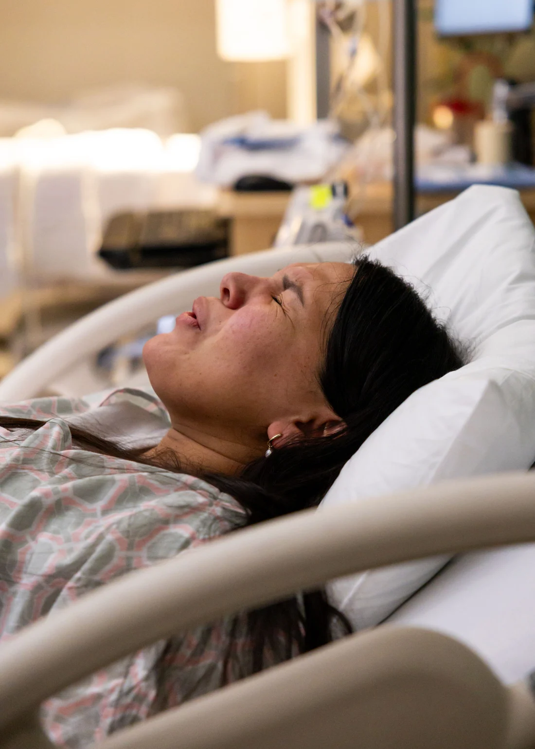 A laboring mother in a hospital gown leans back on the bed with her eyes closed through a contraction